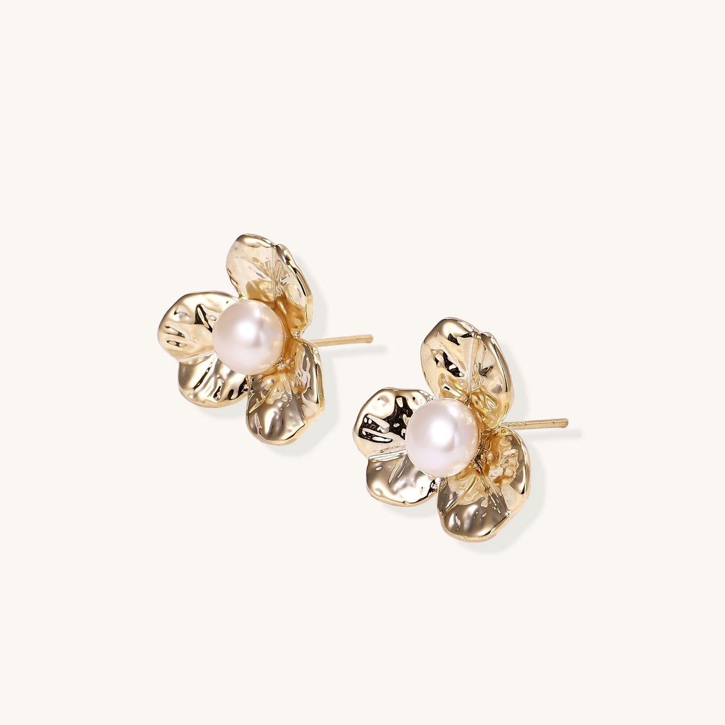 Gold-plated flower stud earrings with freshwater pearl centers on beige background, showing textured petal details.