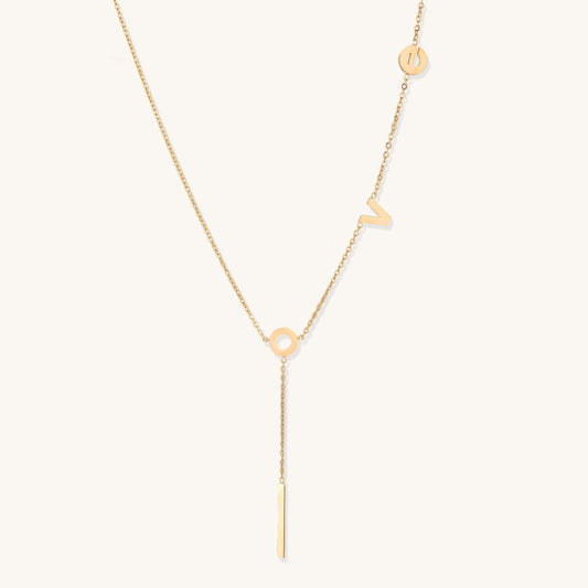 Gold-plated lariat necklace spelling LOVE with letter charms and vertical bar pendant on white background.