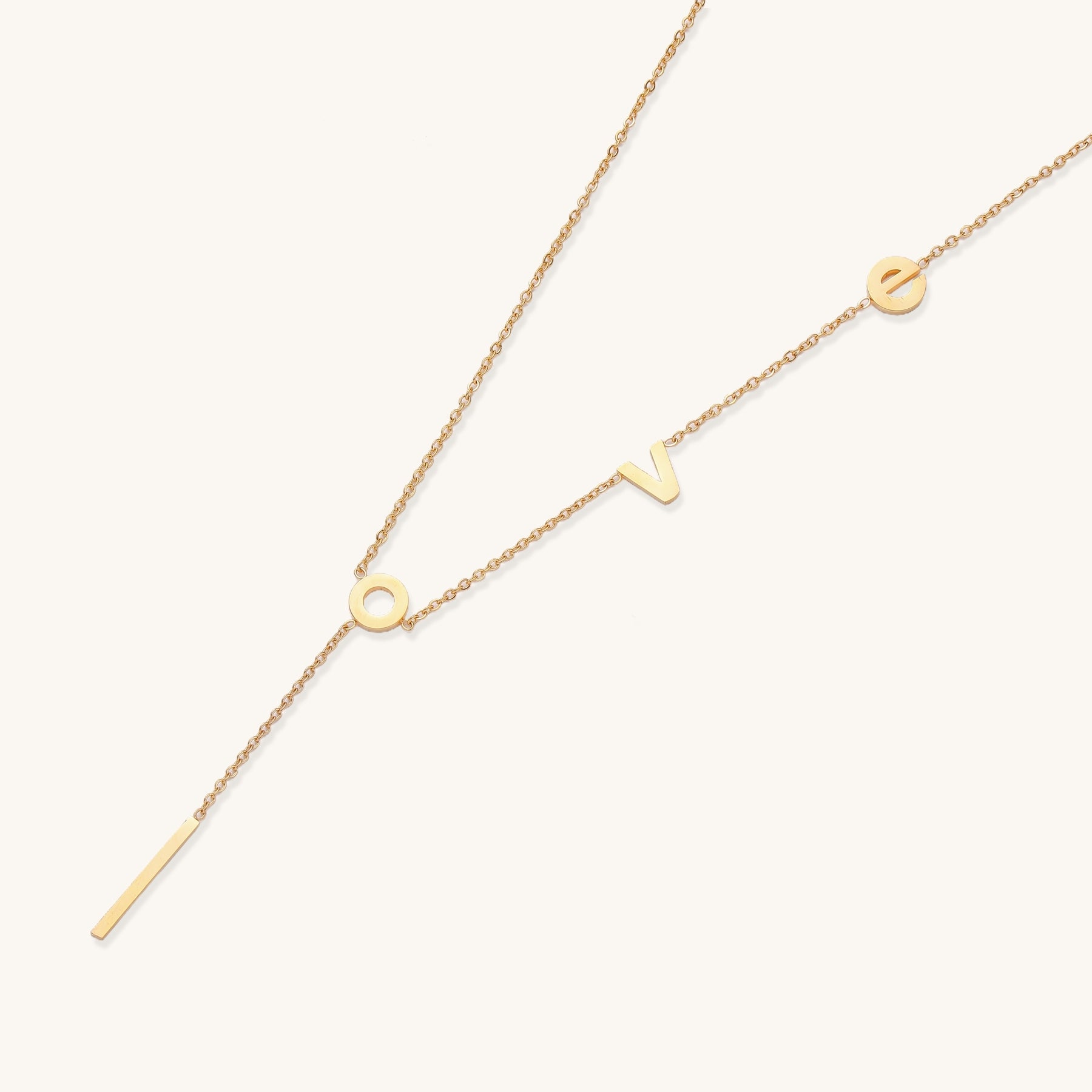 Gold-plated lariat necklace spelling LOVE with letter charms and vertical bar pendant on white background.