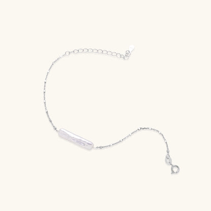 Delicate sterling silver chain bracelet with an organic white baroque pearl centerpiece on neutral background