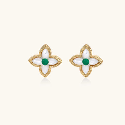 Dainty gold-plated quatrefoil stud earrings with white mother-of-pearl petals and green gemstone centers on beige background.