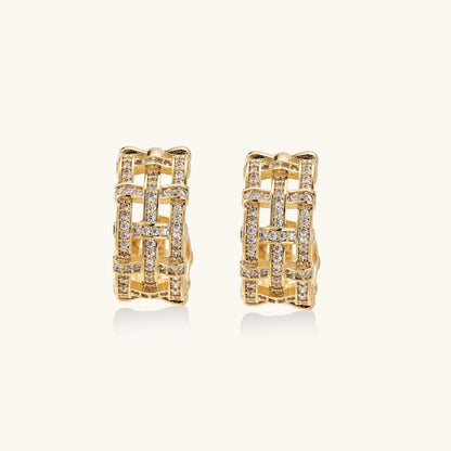 Close-up of geometric gold-plated hoop earrings with crystal pave in intricate lattice pattern on neutral background.