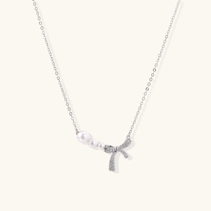 Dainty 14K gold plated necklace with freshwater pearls and sparkling bow charm on white background.