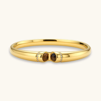 Polished gold bangle with two oval tiger's eye cabochons flanked by pavé diamond accents at center clasp.